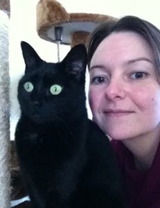Nicola is standing nearby her black cat