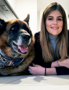Long haired elder dog sitting beside a woman with folded arms